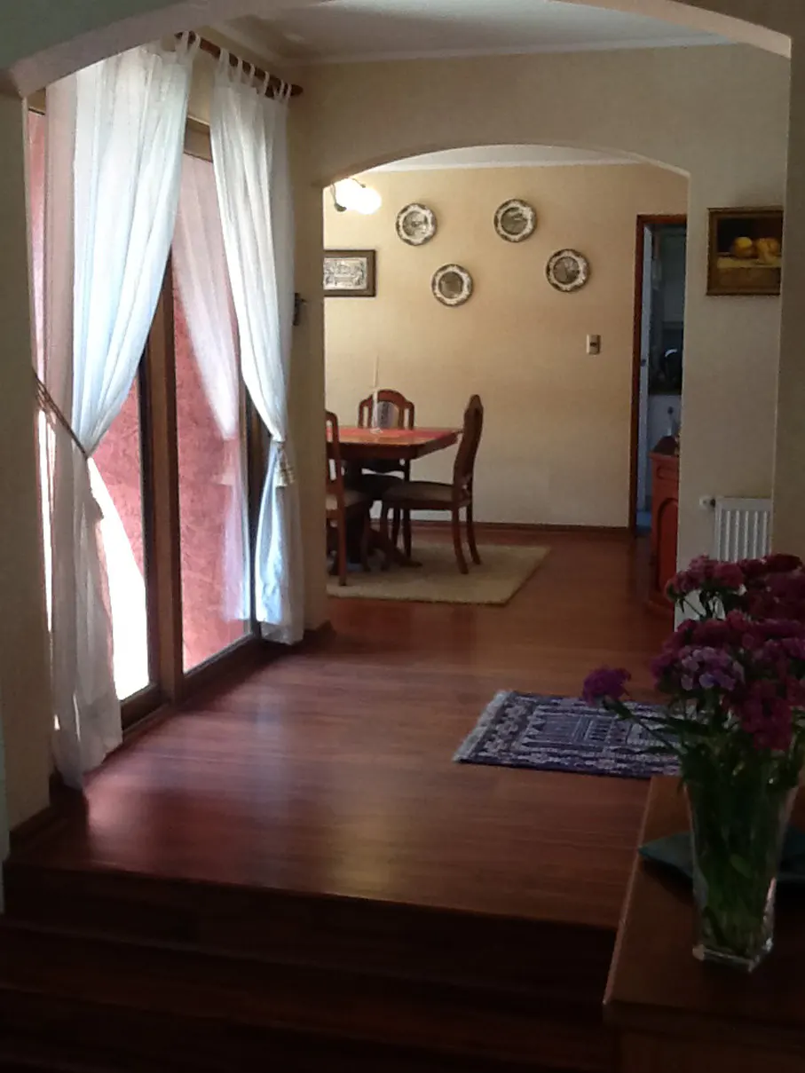 A living room with hardwood floors, a dining room with a table and chairs, and a window with white curtains.