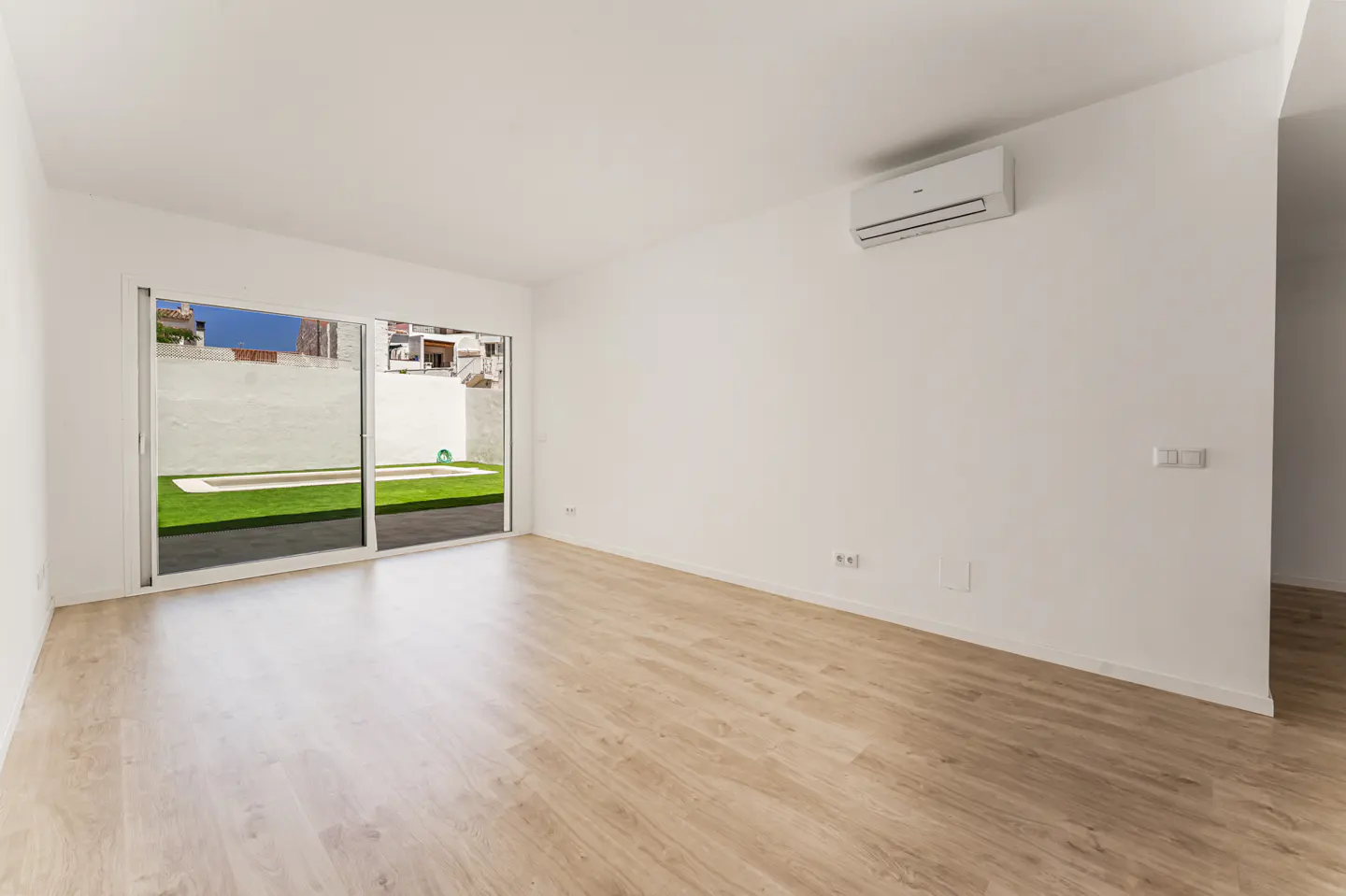 Empty room with light wood floors, white walls, an AC unit, and a sliding glass door opening to a backyard with a pool.