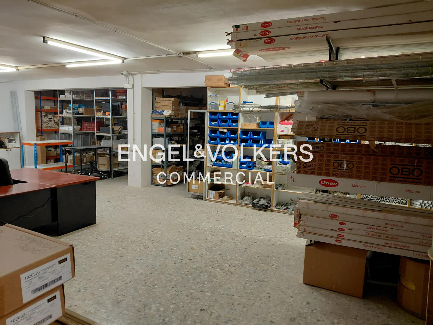 A commercial space with shelves stocked with various items, a desk, and boxes on the floor.