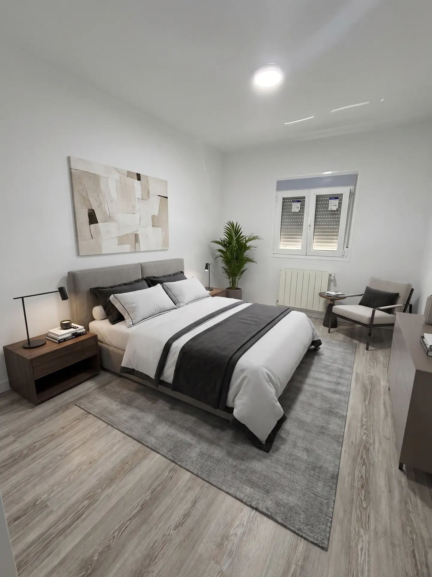 Bright bedroom with a gray bed, white linens, and a gray throw. A gray rug covers the wood floor. A window and chair are in the background.