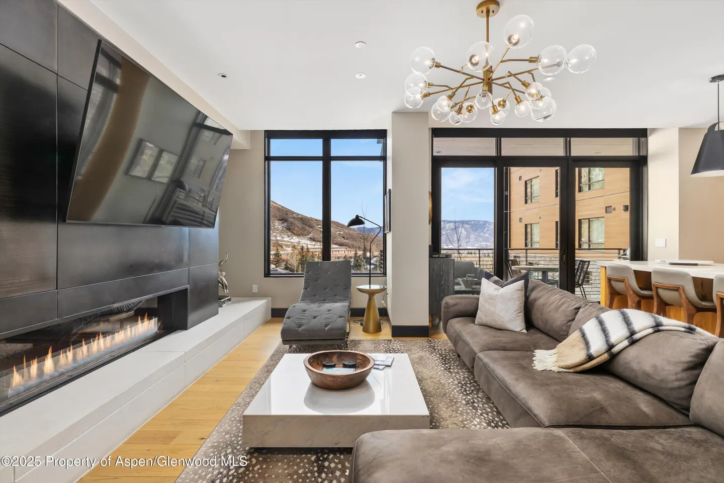 Modern living room with a large sectional sofa, linear fireplace, white coffee table, and mountain views through windows.