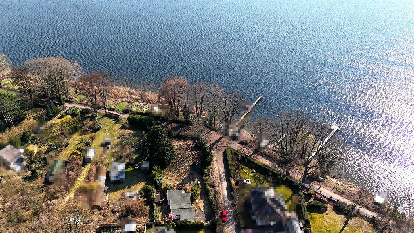 Aerial view of lakefront properties with docks, trees, and a red car on a road.