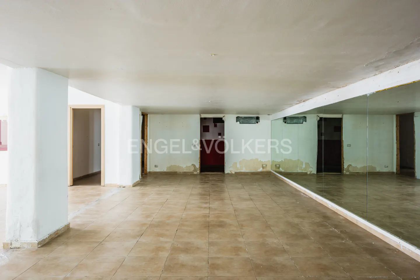 Empty room with tile floor, white walls, and a large mirror. Doorways are visible. Engel & Volkers logo is superimposed.