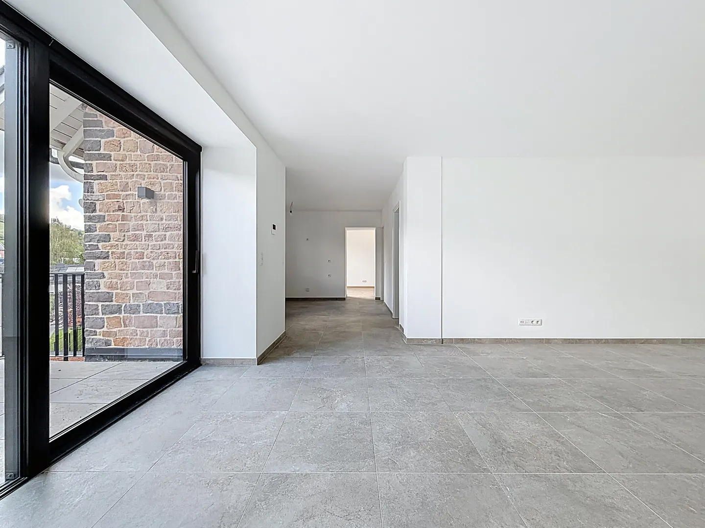 Empty room with gray tile floor, white walls, and black-framed sliding glass door to a brick patio.