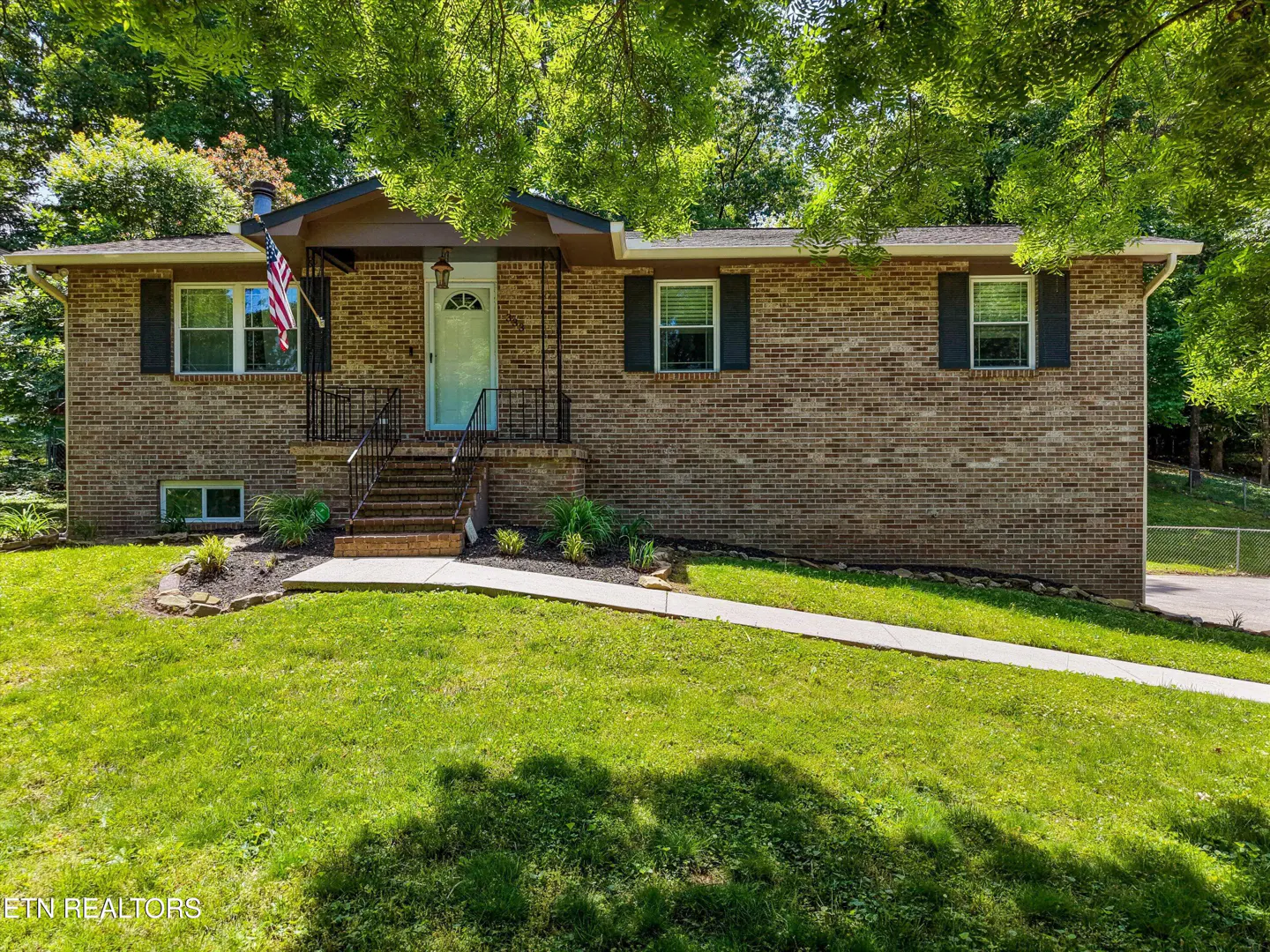 A tan brick house with a light blue door, black shutters, and an American flag on the front porch.