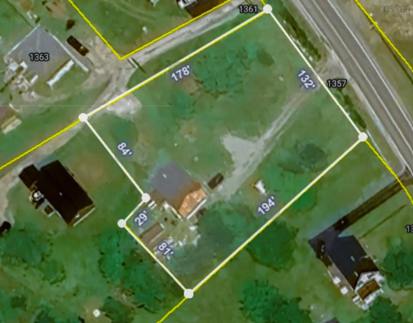 Aerial view of a property outlined in white with dimensions labeled in feet, surrounded by green grass and other buildings.