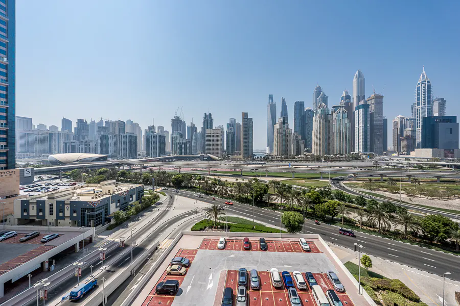 High-angle view of a Dubai cityscape with a parking lot in the foreground, multi-lane roads, and modern skyscrapers.