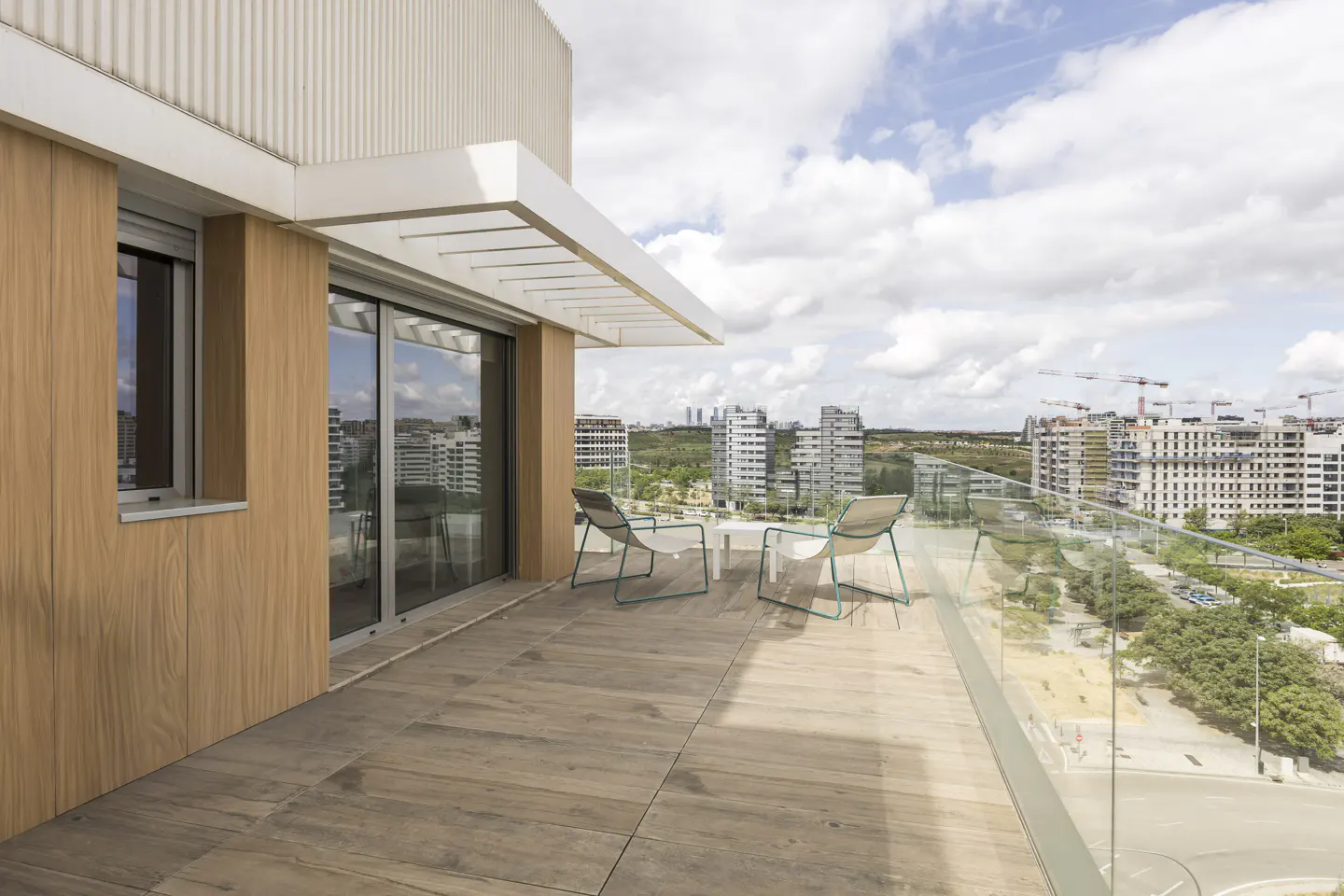 Balcony view with two chairs and a small table overlooking a city skyline on a sunny day.