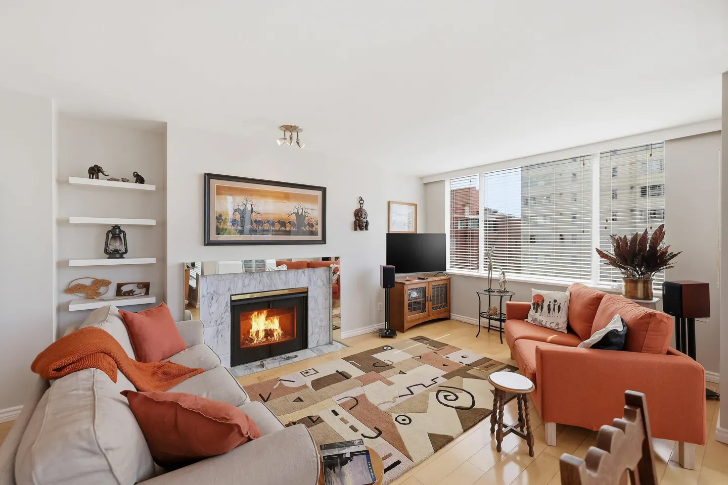 Living room with a fireplace, orange sofa, and beige sofa. Shelves with decor, a TV, and a patterned rug are also visible.