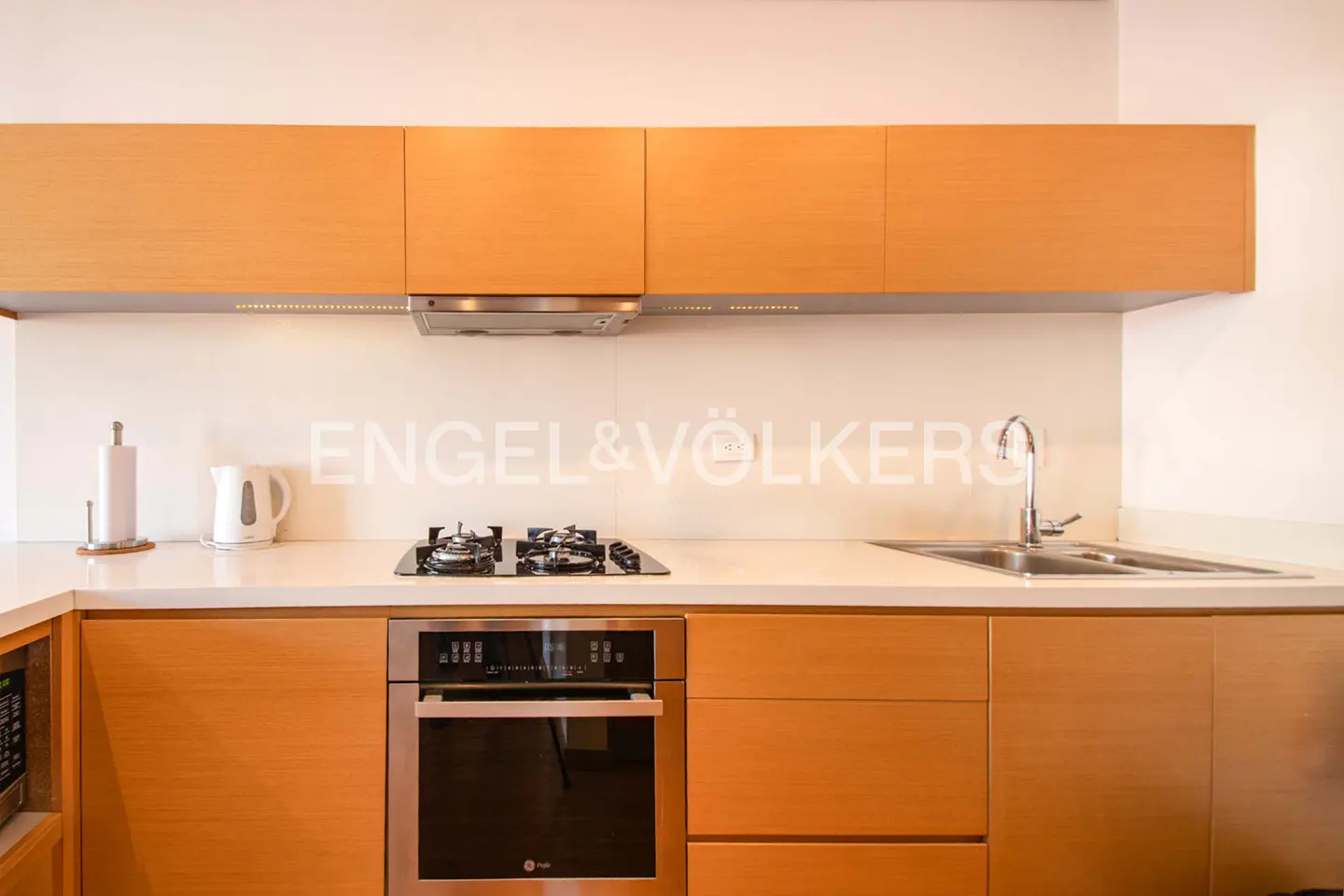 Modern kitchen with light wood cabinets, white countertops, a gas stovetop, stainless steel oven, and a sink.