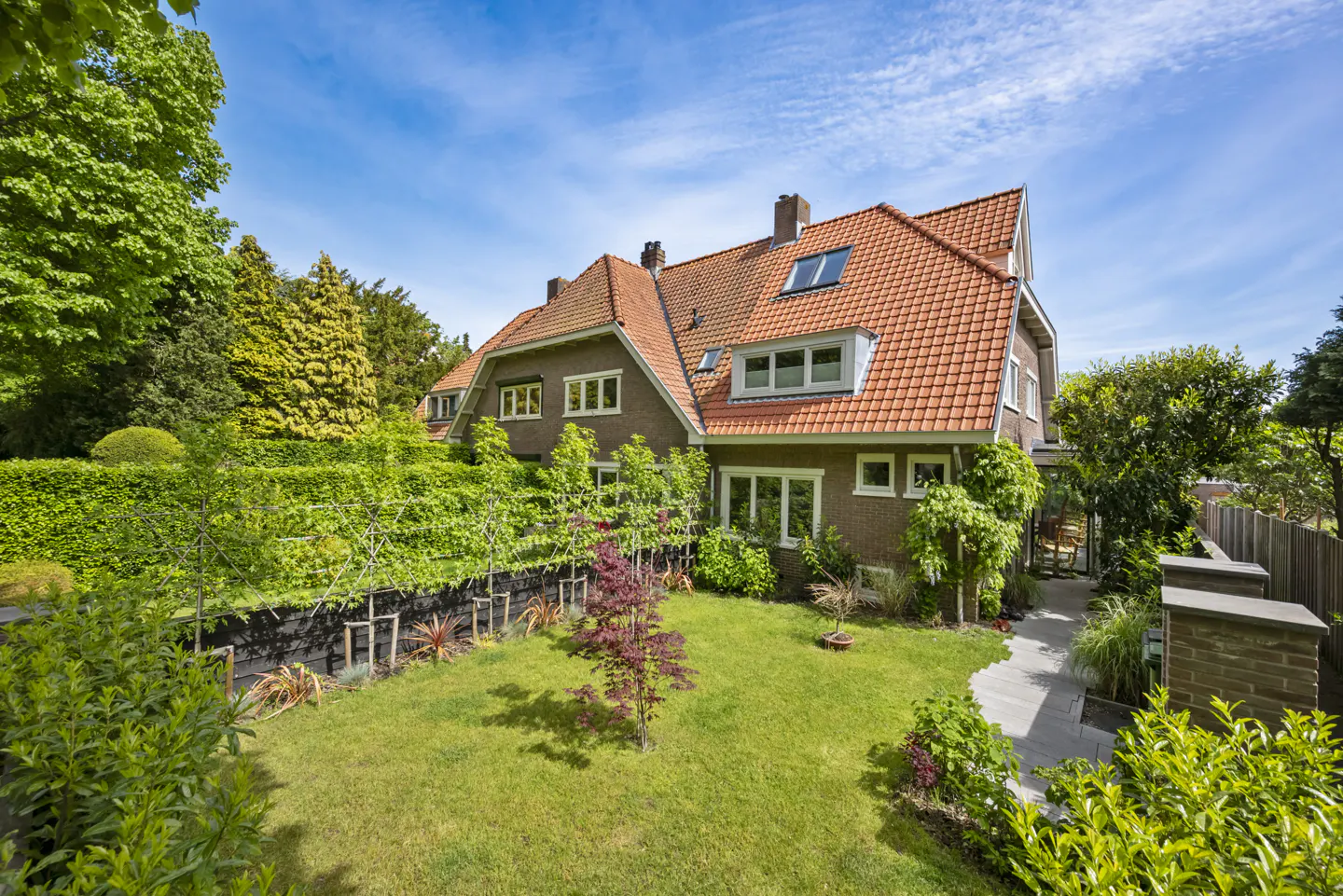 A two-story house with a red tile roof and a green lawn under a blue sky.