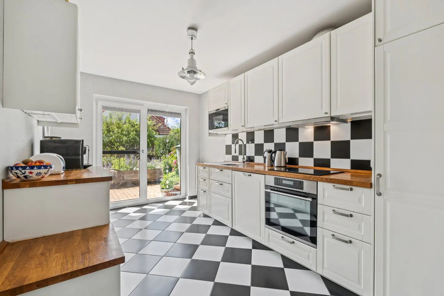 Modern kitchen with white cabinets, wood countertops, black and white checkered floor and backsplash, and a glass door.