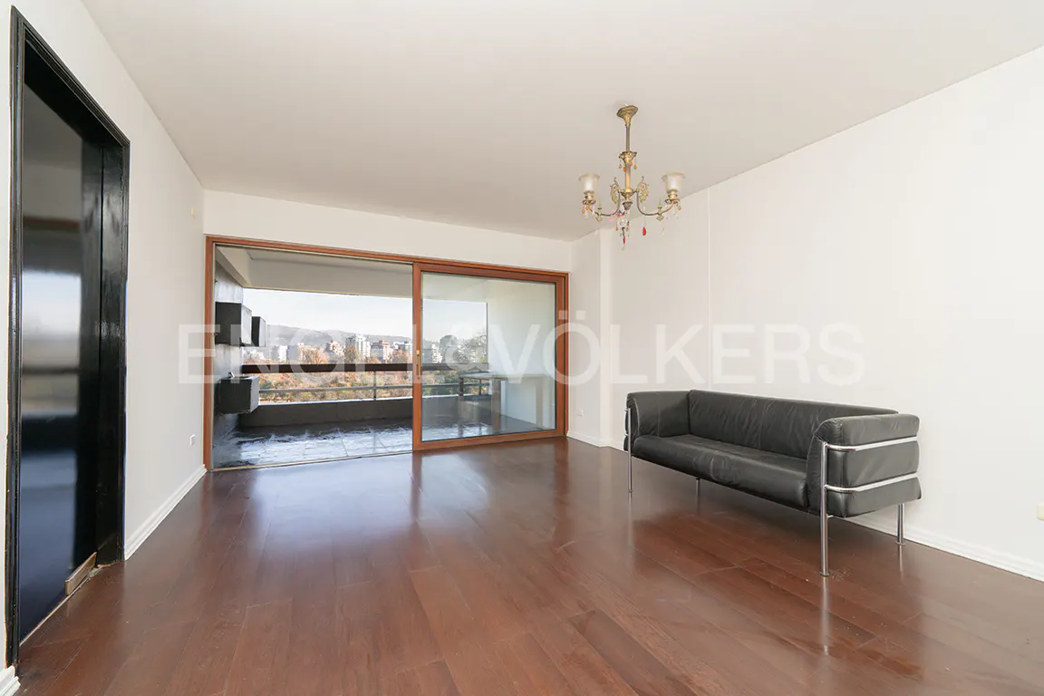 Minimalist living room with dark wood floors, a black leather sofa, a chandelier, and a balcony with city views.