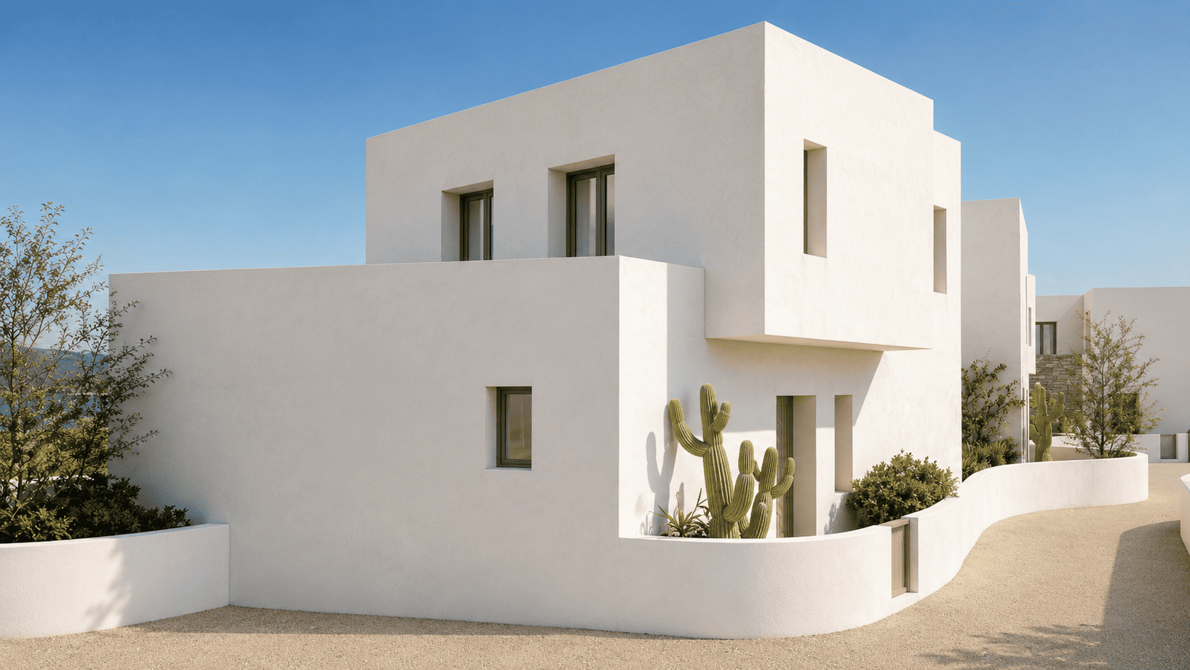 Modern white minimalist villa with geometric architecture, a curved wall, and a cactus garden under a clear blue sky.