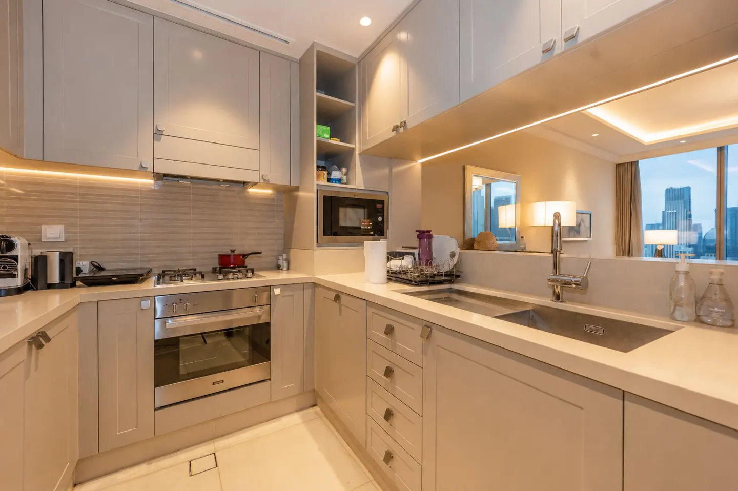 A modern kitchen with beige cabinets, stainless steel appliances, and a sink overlooking a city skyline.