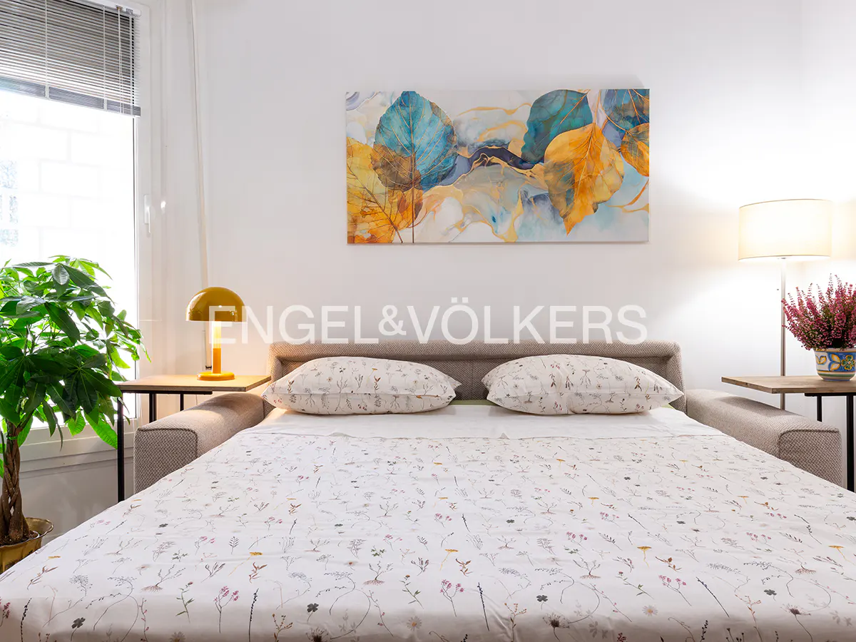 Bedroom with a bed covered in a floral pattern, pillows, and a painting of leaves above the headboard.