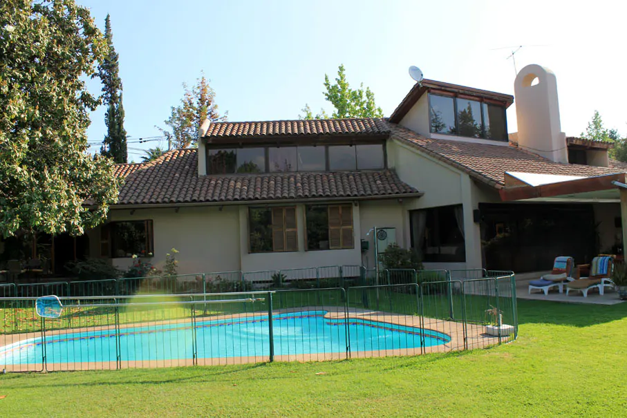 Beige house with a red tile roof, a pool with a green fence, and green grass.
