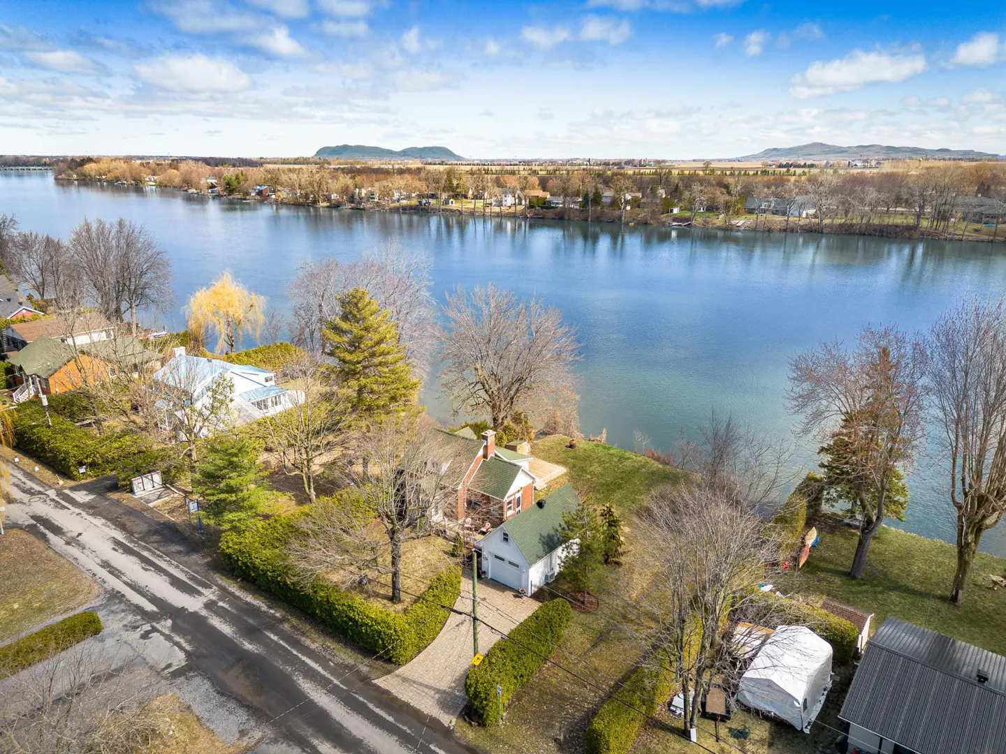 Aerial view of a red and white house with a green roof, next to a blue river under a blue sky with white clouds.