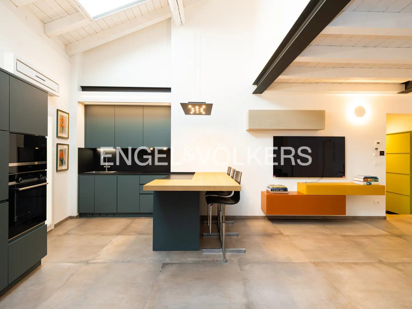 A modern kitchen and living area with gray cabinets, a wood countertop island, and colorful shelving.