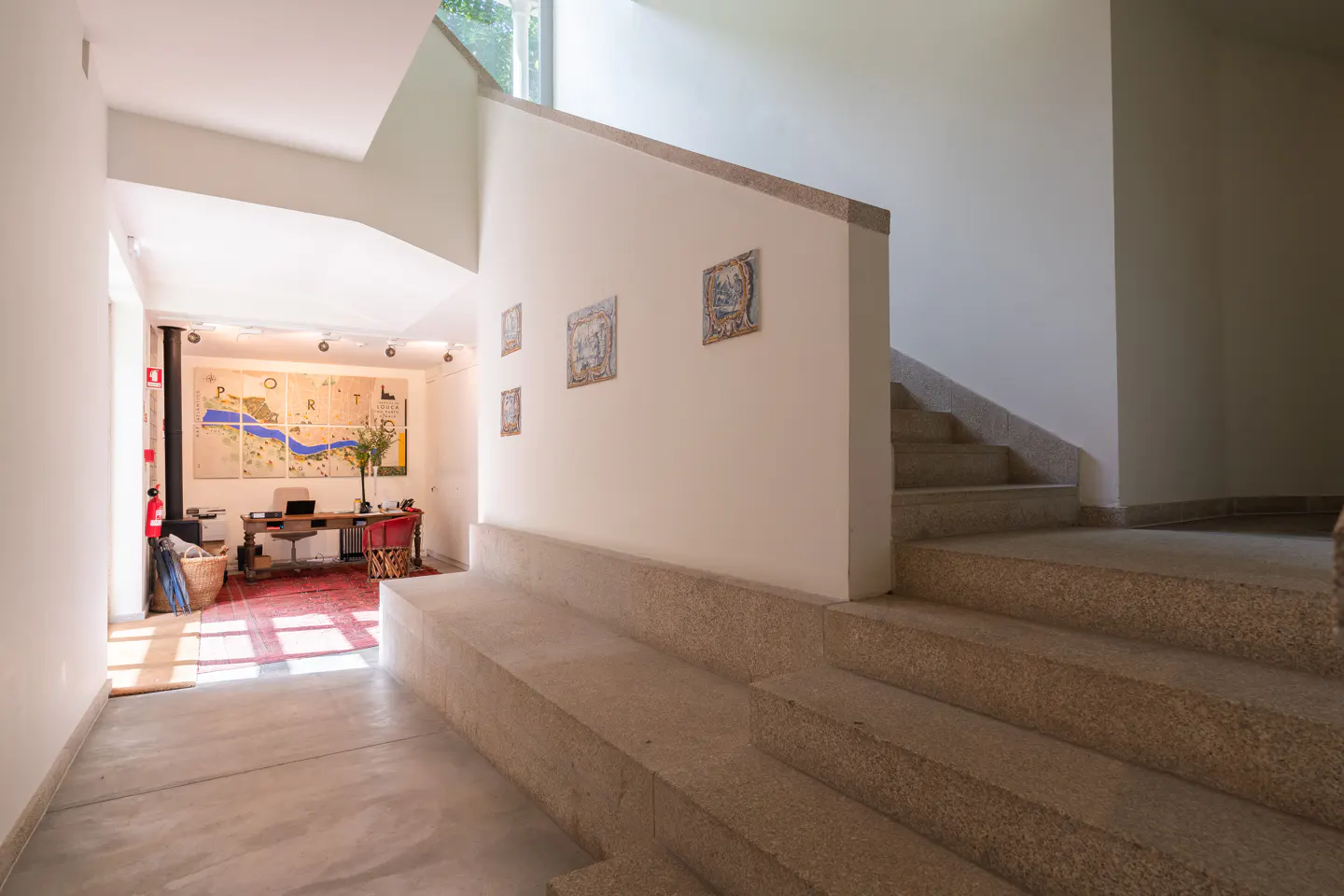 Interior view of a modern home with stone stairs, white walls with tile art, and a study area with a desk and map art.