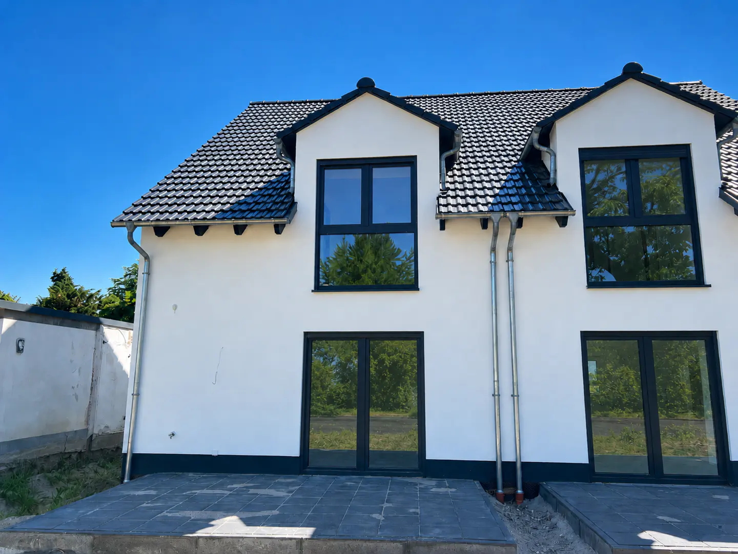 Exterior of a two-story white house with black trim, windows, and a dark gray tiled roof under a clear blue sky.