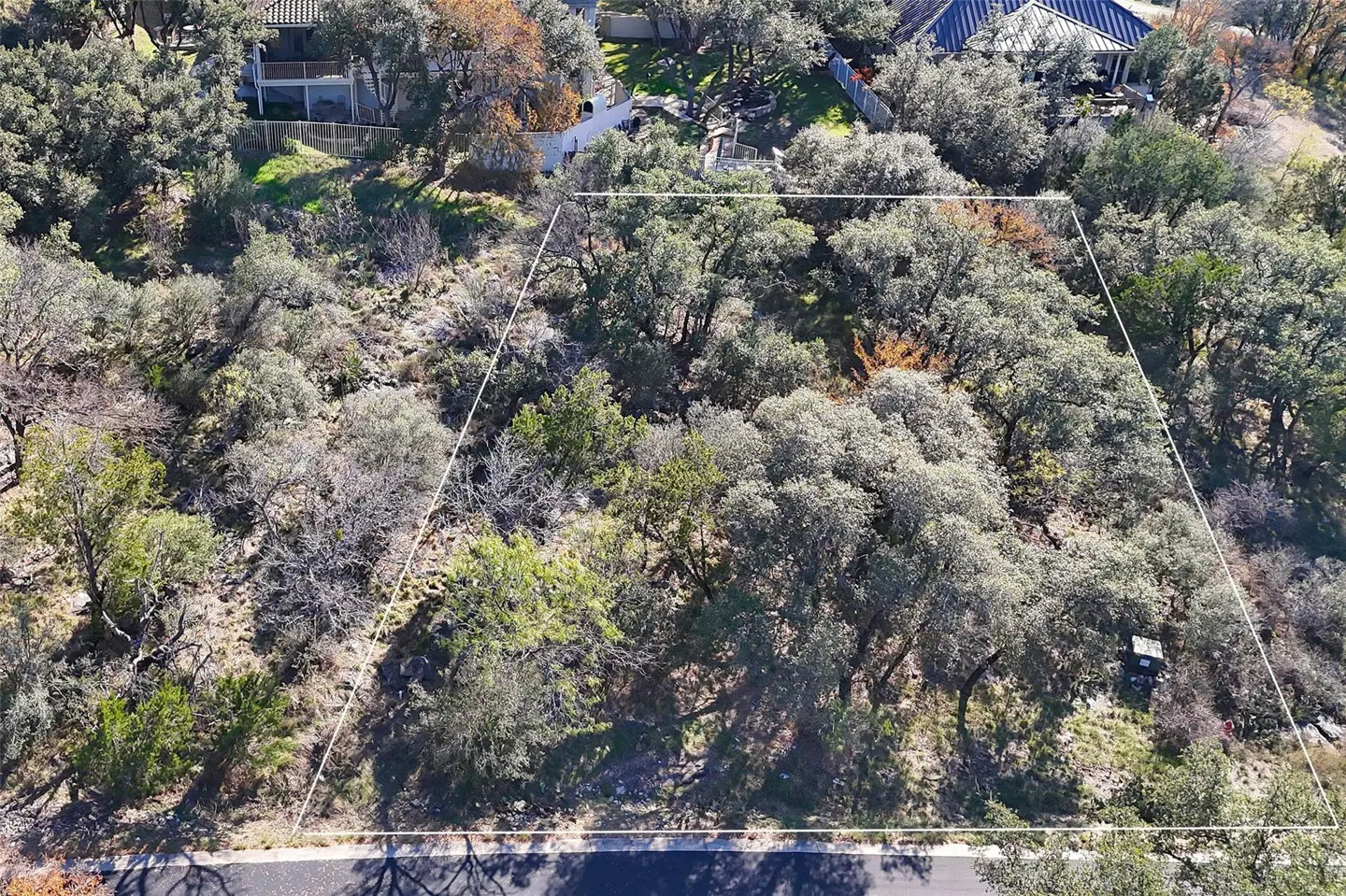 Aerial view of a wooded lot outlined in white, with houses visible in the background.