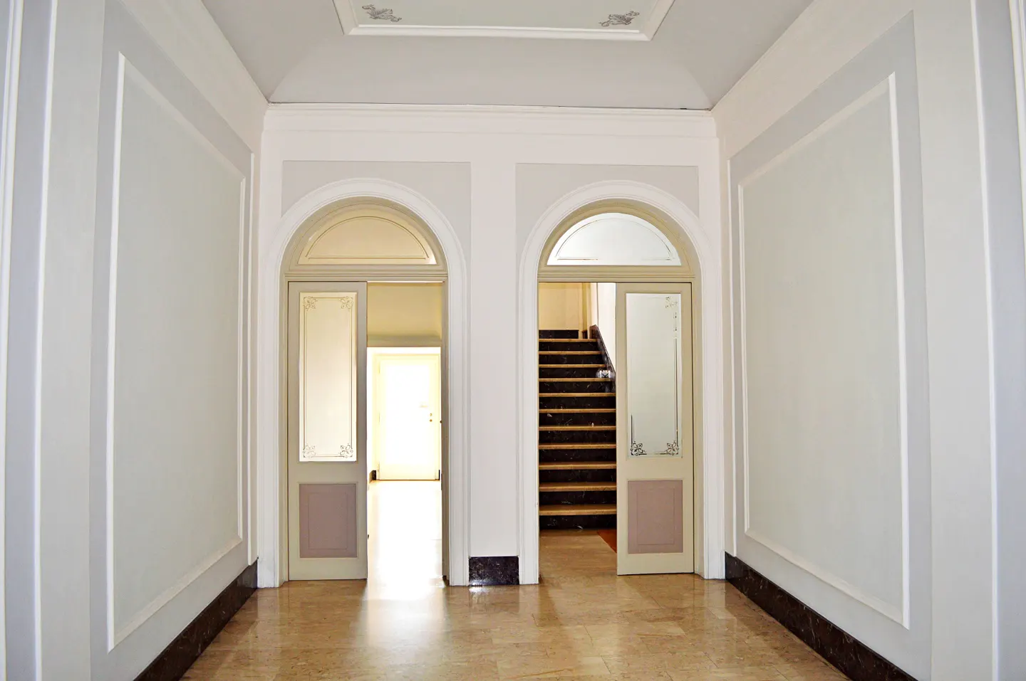 Hallway with marble floor, white walls, and two arched doorways. One doorway leads to stairs, the other to a bright room.