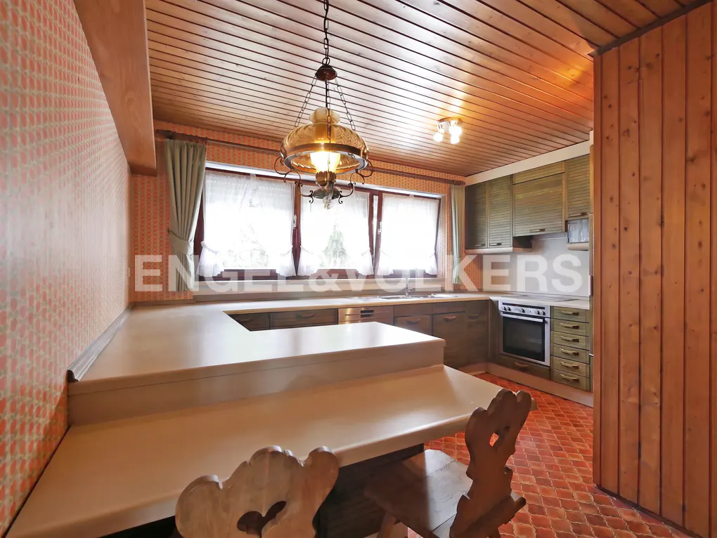 A kitchen with wood paneling, a large island, and a hanging light fixture.