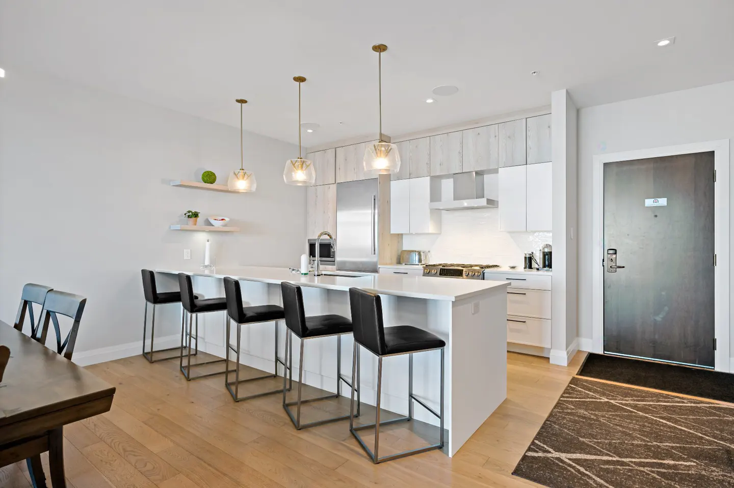 Bright, modern kitchen with white cabinets, island with black stools, and wood floors. Three pendant lights hang above the island.