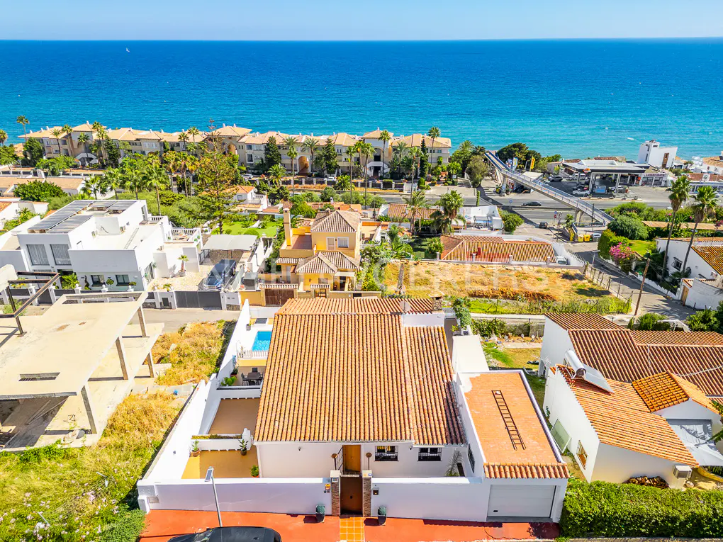 Aerial view of a white house with a red tile roof, a pool, and the ocean in the background.