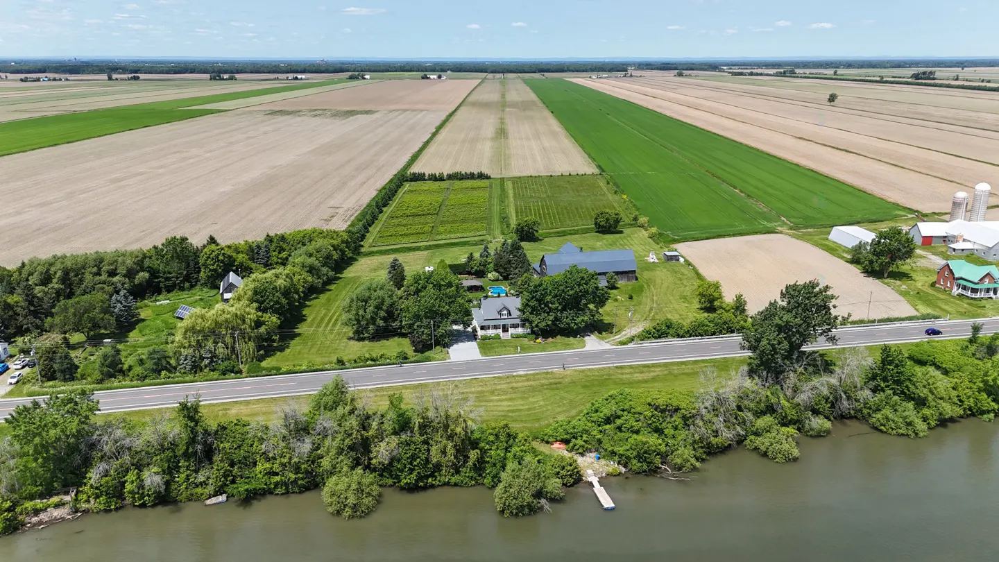 Aerial view of a rural landscape with fields, a farmhouse, and a waterfront property on a sunny day.