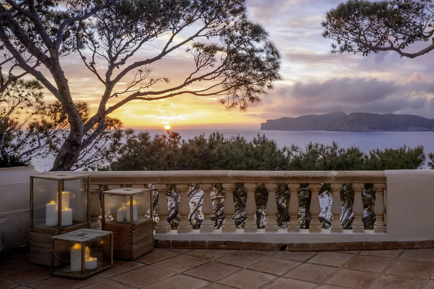 Balcony view at sunset with candles. Ocean and island in background. Warm orange and pink sky.