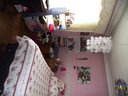 Bedroom with pink walls, a bed with a floral pattern, a desk, and a white flower-shaped lamp.