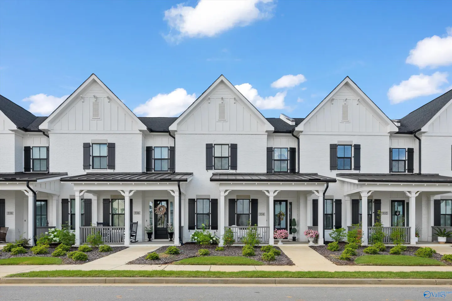 Row of three-story white townhouses with black shutters and front porches under a blue sky.