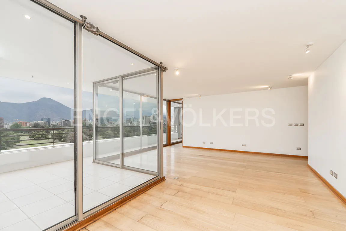 Bright, empty room with wood floors and white walls. Large glass doors open to a balcony with a city and mountain view.