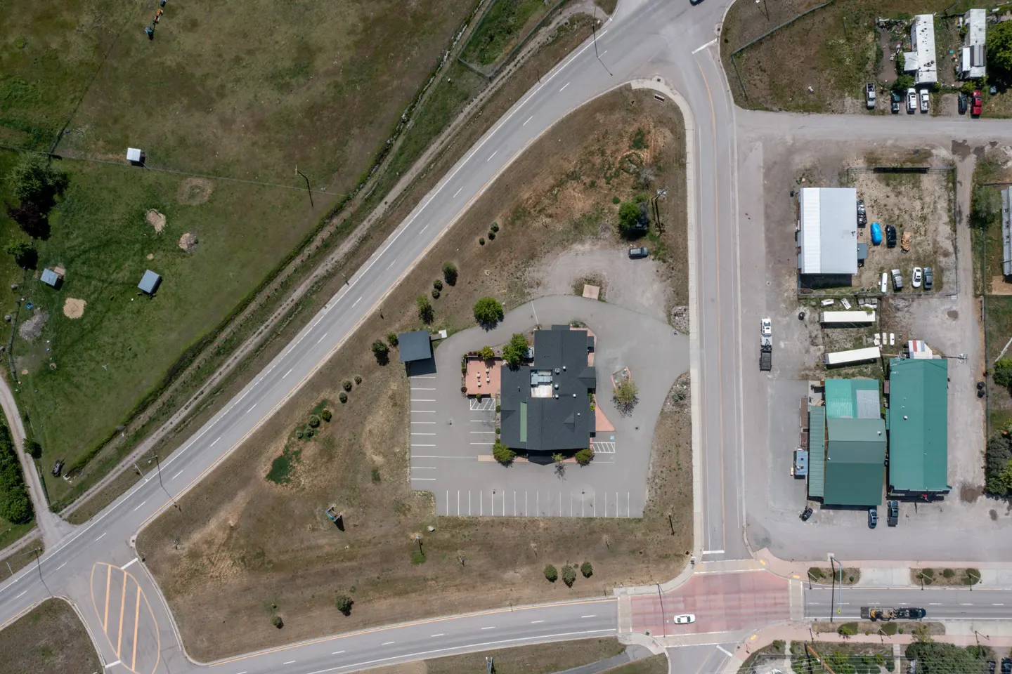 Aerial view of a commercial building with a dark roof and parking lot, surrounded by roads, grass, and other buildings.