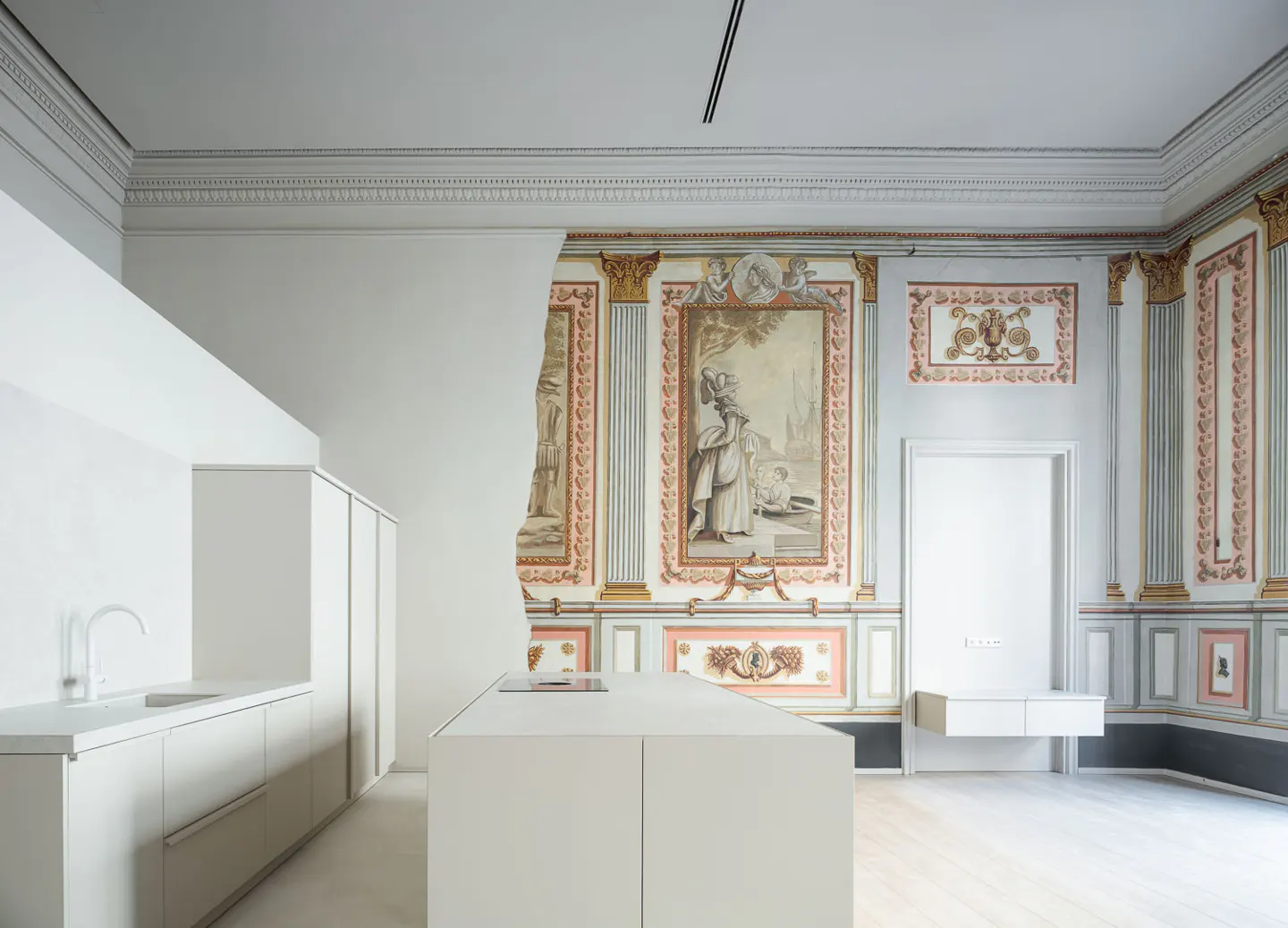 A modern white kitchen in a room with ornate, antique wall paintings.