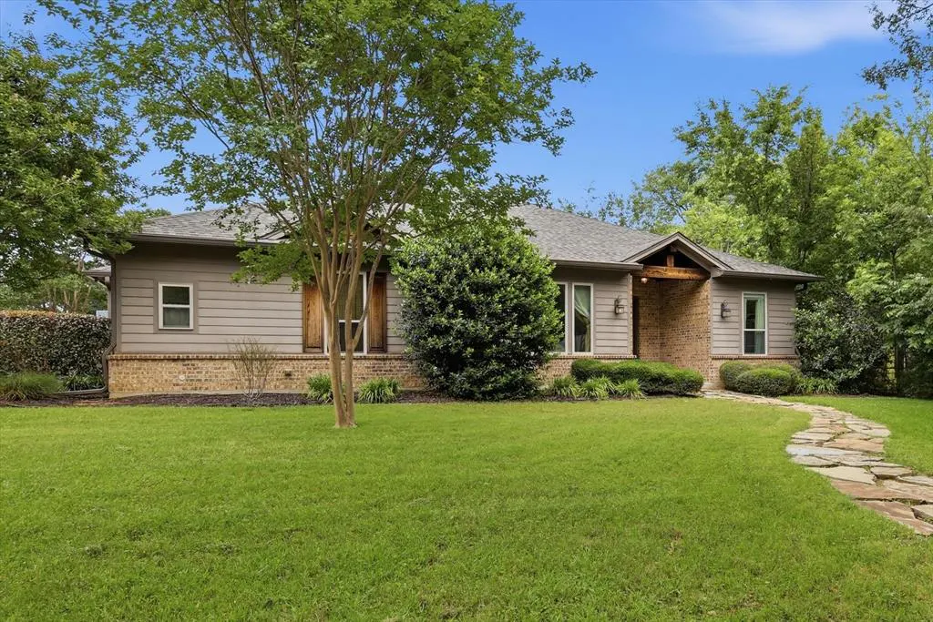 A single-story home with gray siding, brick accents, and a stone walkway on a green lawn under a blue sky.