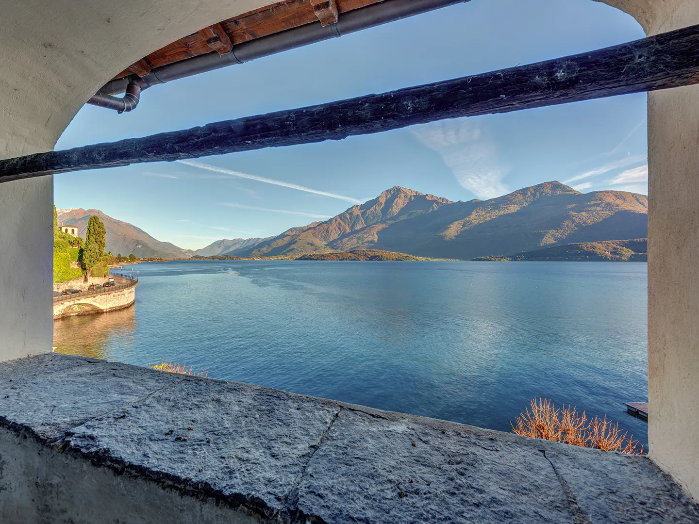 View of a blue lake and mountains through a stone archway. The sky is blue with faint contrails.