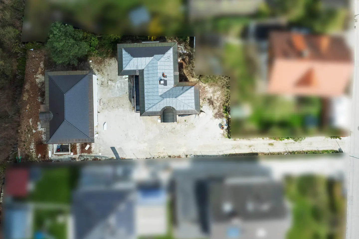Aerial view of a house with a gray roof, a smaller building, and a yard with trees.