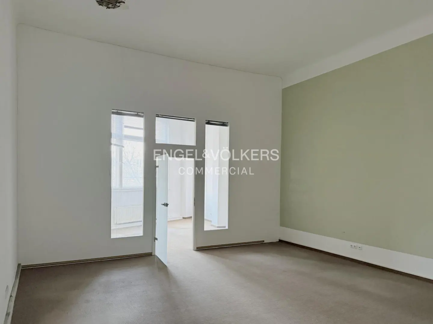 Empty room with white and light green walls, brown floor, and open door with Engel & Völkers logo.