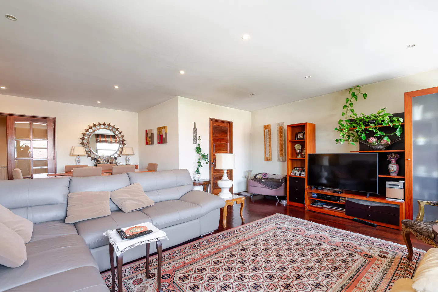 Spacious living room with a grey sectional sofa, patterned area rug, wooden media console, and a large sunburst mirror.