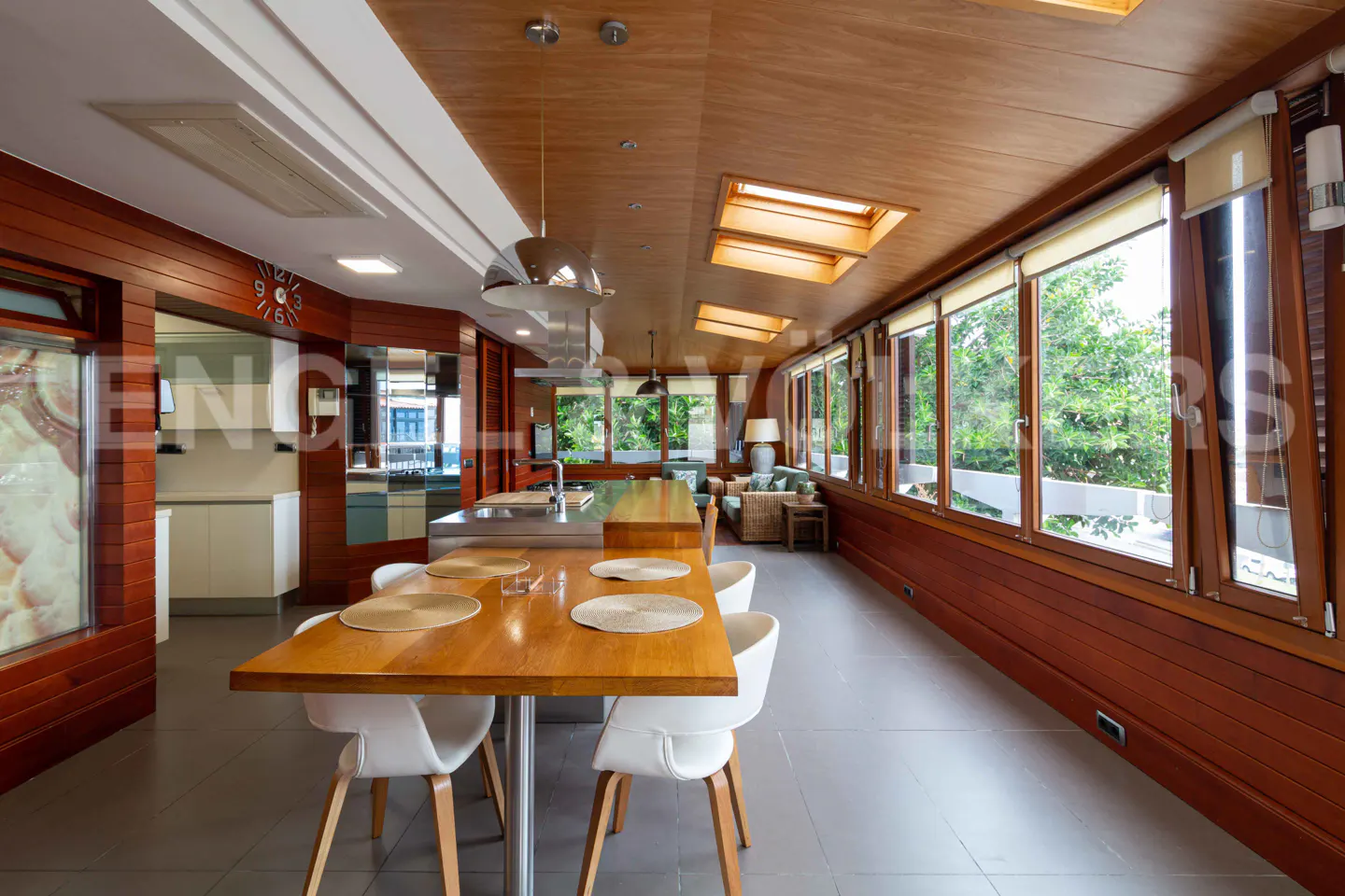 A modern kitchen and dining area with wood paneling, large windows, and white chairs.