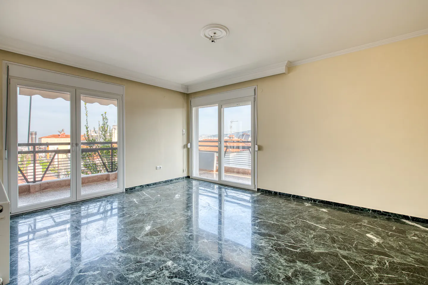 Empty room with marble floor, cream walls, and two sets of white sliding glass doors to balconies.