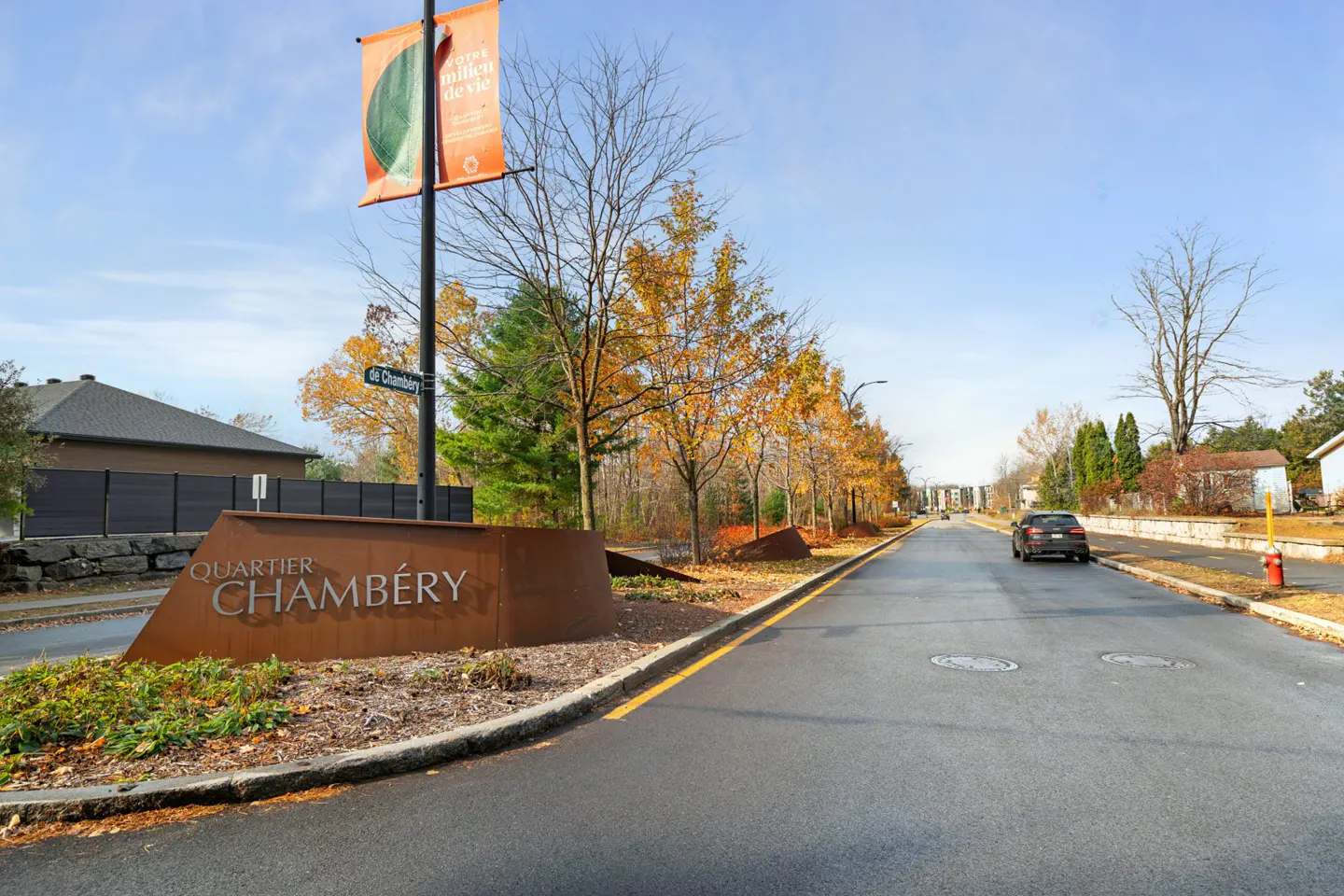 Street view of Quartier Chambery with a brown sign, trees with yellow leaves, and a car driving down the road.