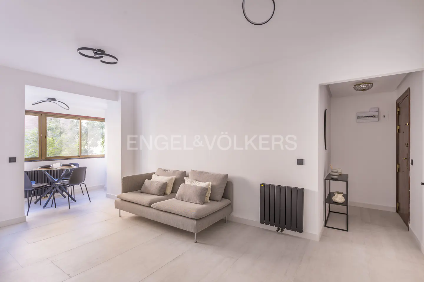 Bright, modern apartment interior with a gray sofa, dining table, and black radiator against white walls.