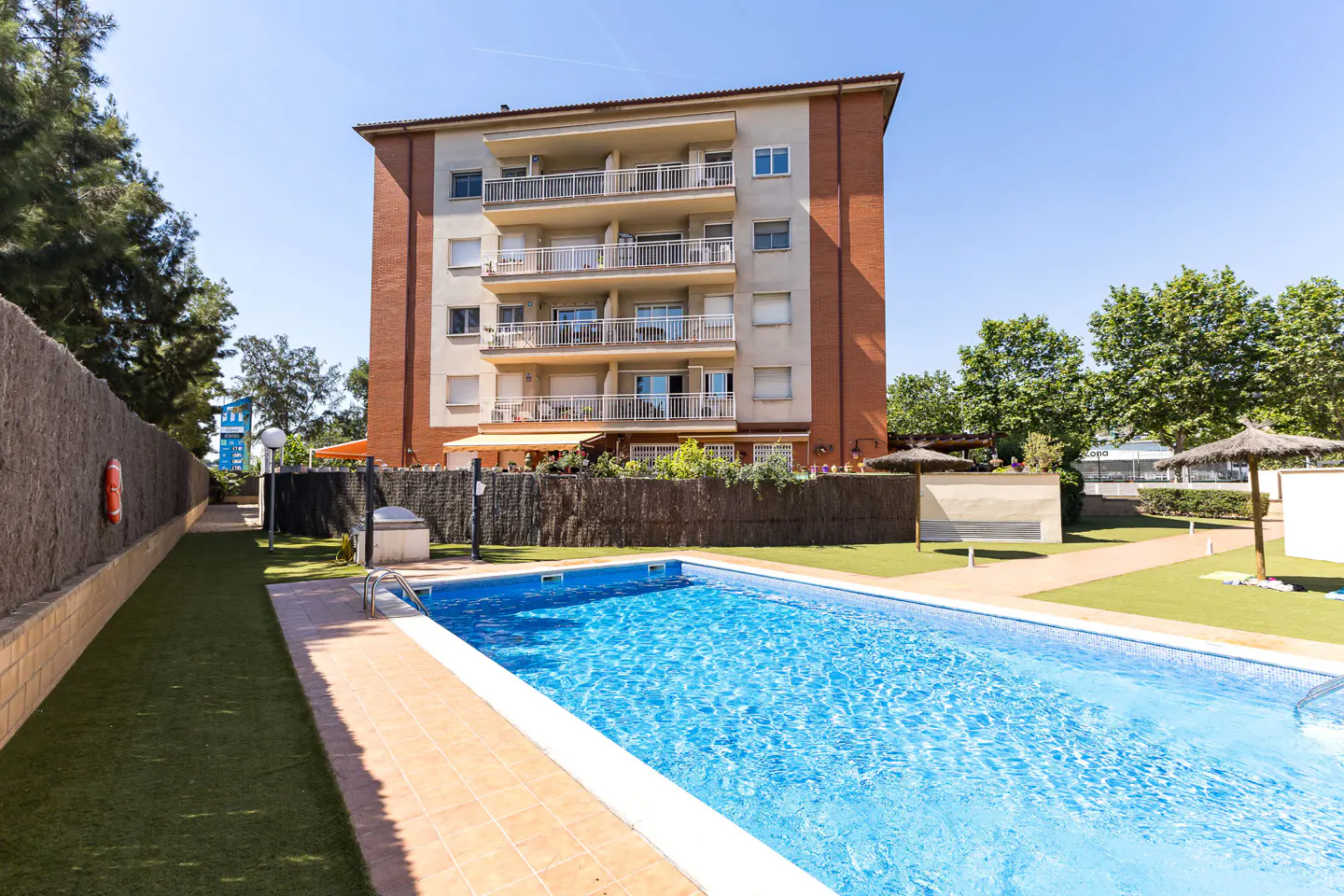 Exterior view of a brick and beige apartment building with balconies, a pool, and a grassy area.