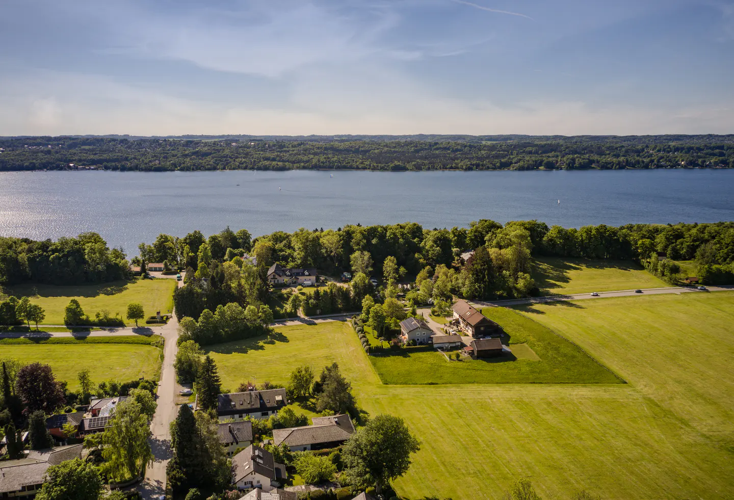 Aerial view of houses and green fields near a lake under a blue sky.