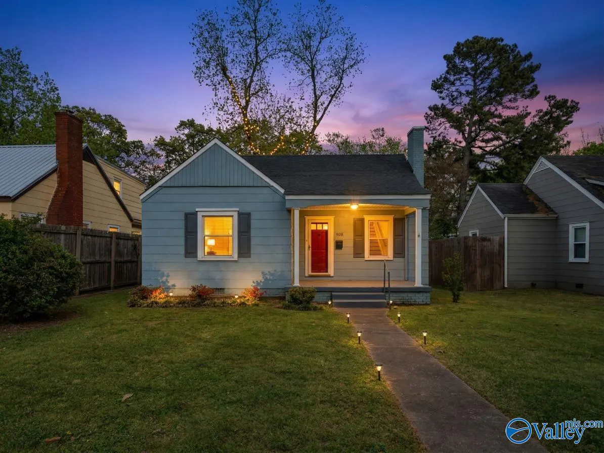 Exterior of a blue single-story home with a red front door at dusk. A walkway leads to the house, lit by small lights.