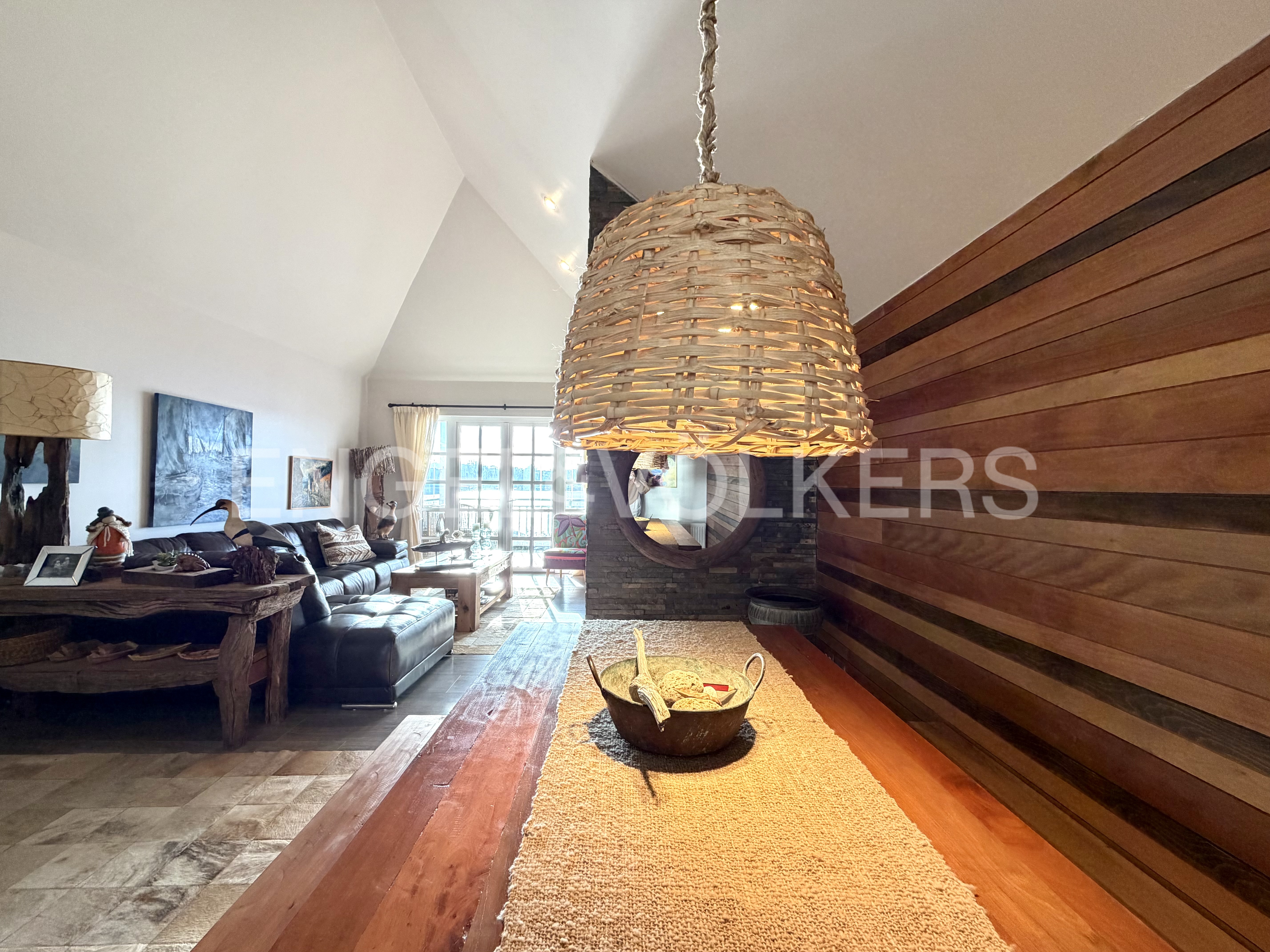 A rustic dining area with a woven pendant light over a wooden table, featuring a wood-paneled wall and a cozy living room. [AI-generated text]